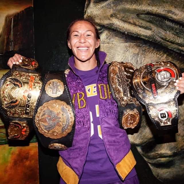 Chris Cyborg holding up her 4  different promotional belts.
